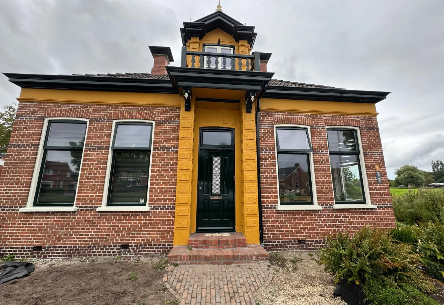 Vrijstaand huis in Usquert met okergeel geschilderd siermetselwerk, donkergroene kozijnen en een zwart gelakte daklijst met torentje